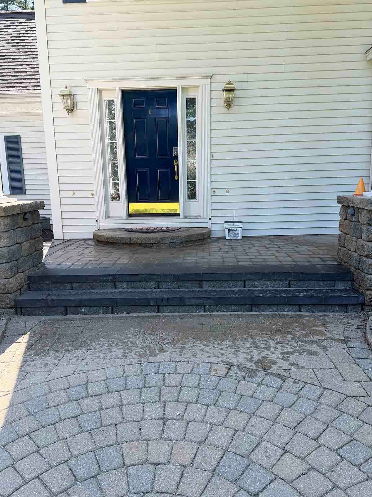 Front entrance with blue door, short steps, and stone walkway leading to a white house