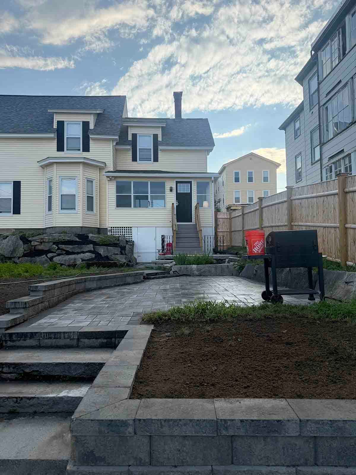 Front yard with stone steps, paved path, patchy lawn, and a house under a cloudy sky.
