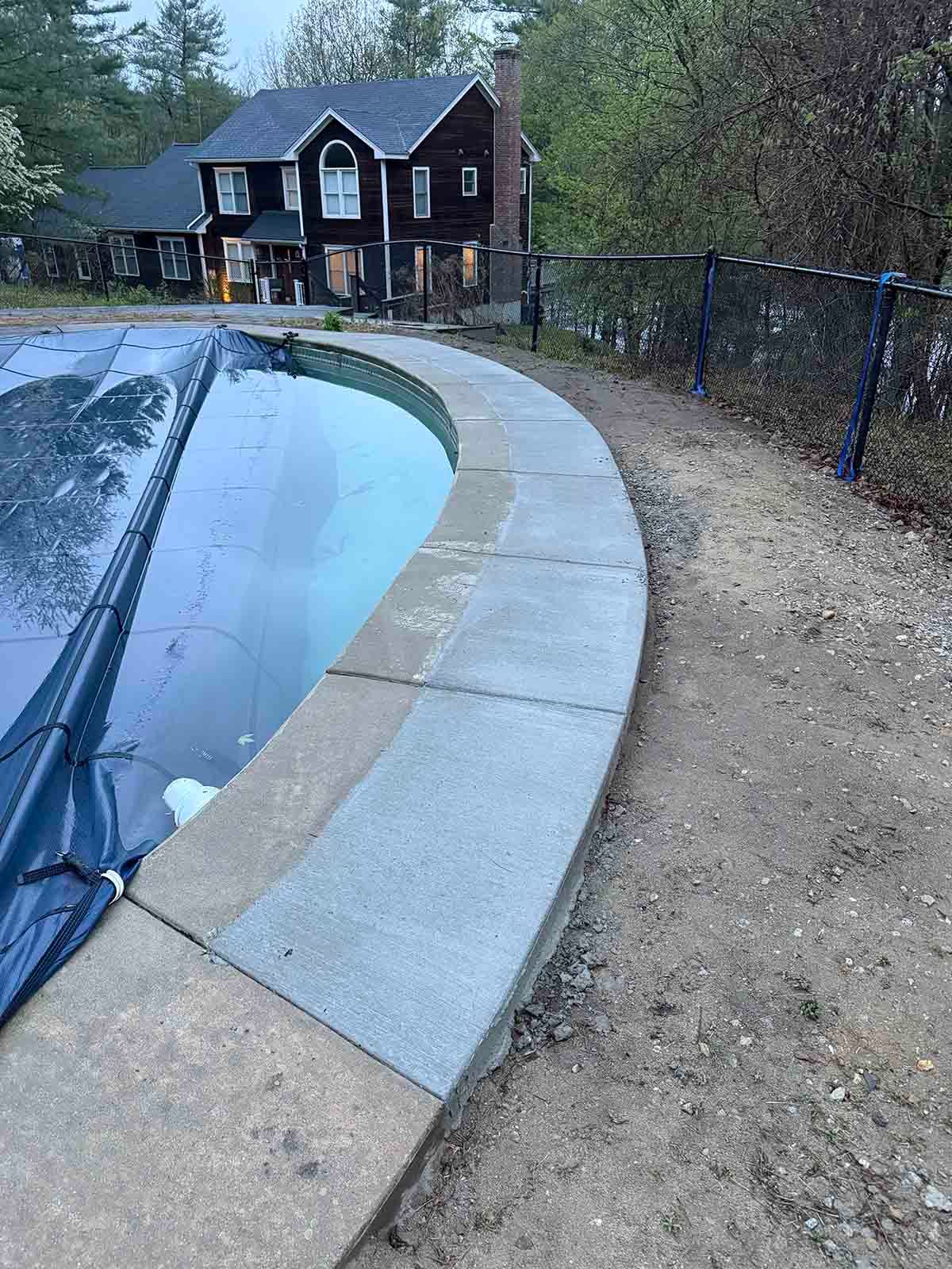Curved pool edge with black cover in a backyard, beside a gravel path and house in the background