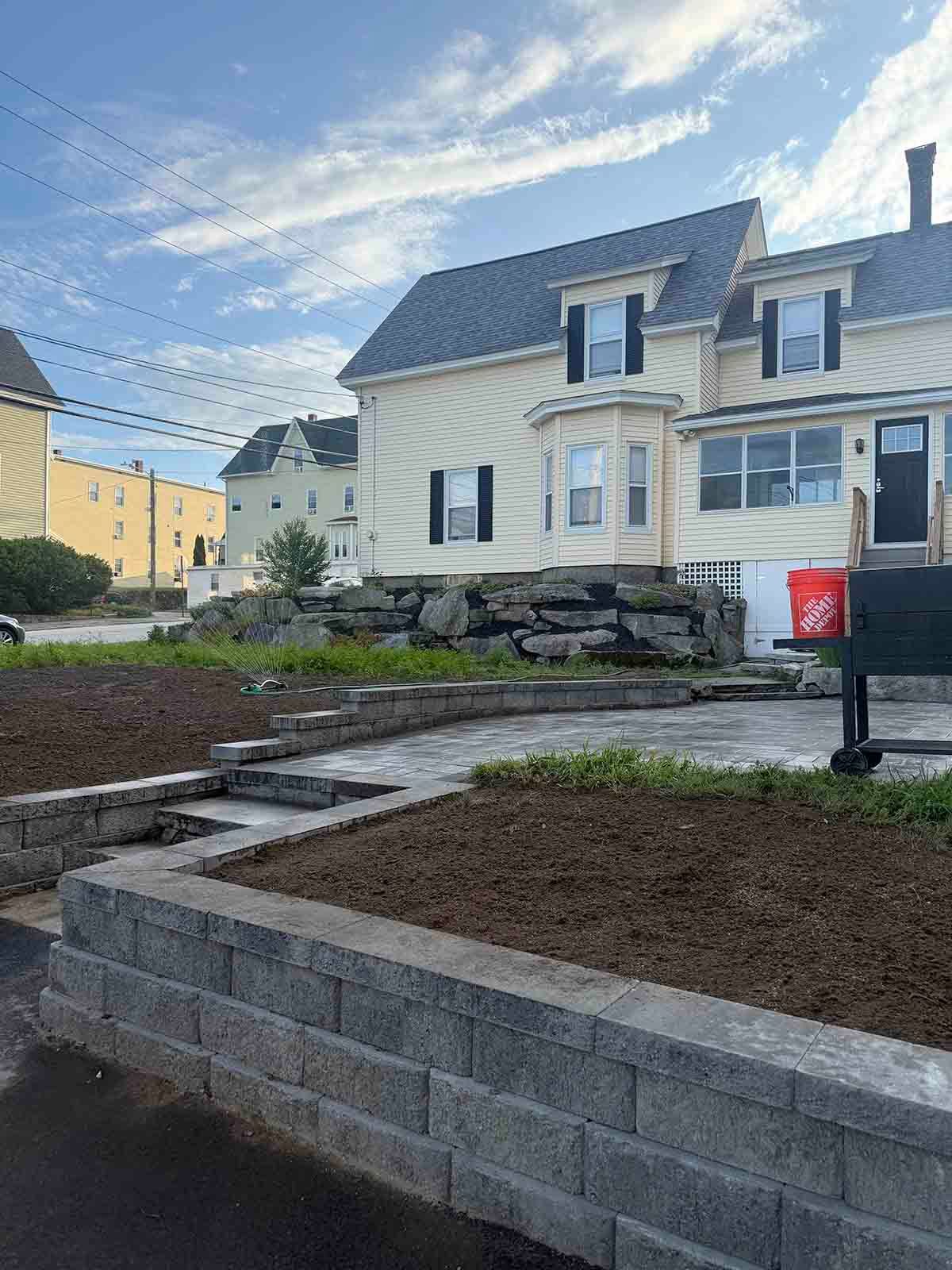 Newly built stone retaining walls and a walkway beside beige row houses under a blue sky