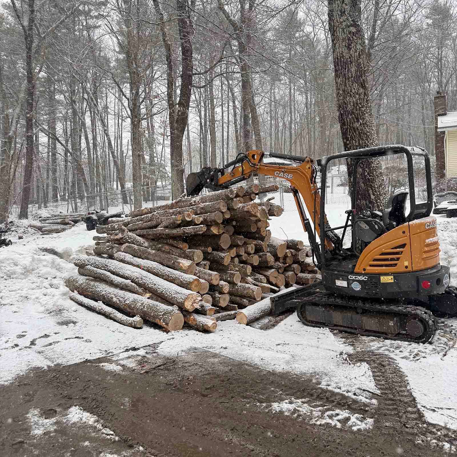 Orange excavator stacking logs in a snowy forest clearing
