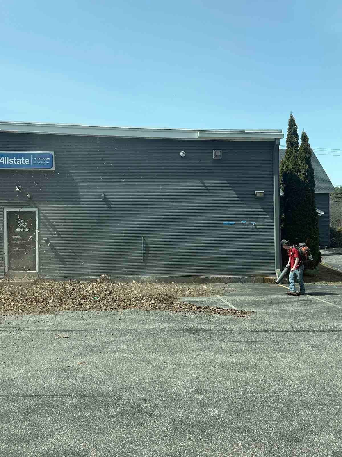 Two people walking beside a dark gray building with a blue sign on a sunny day