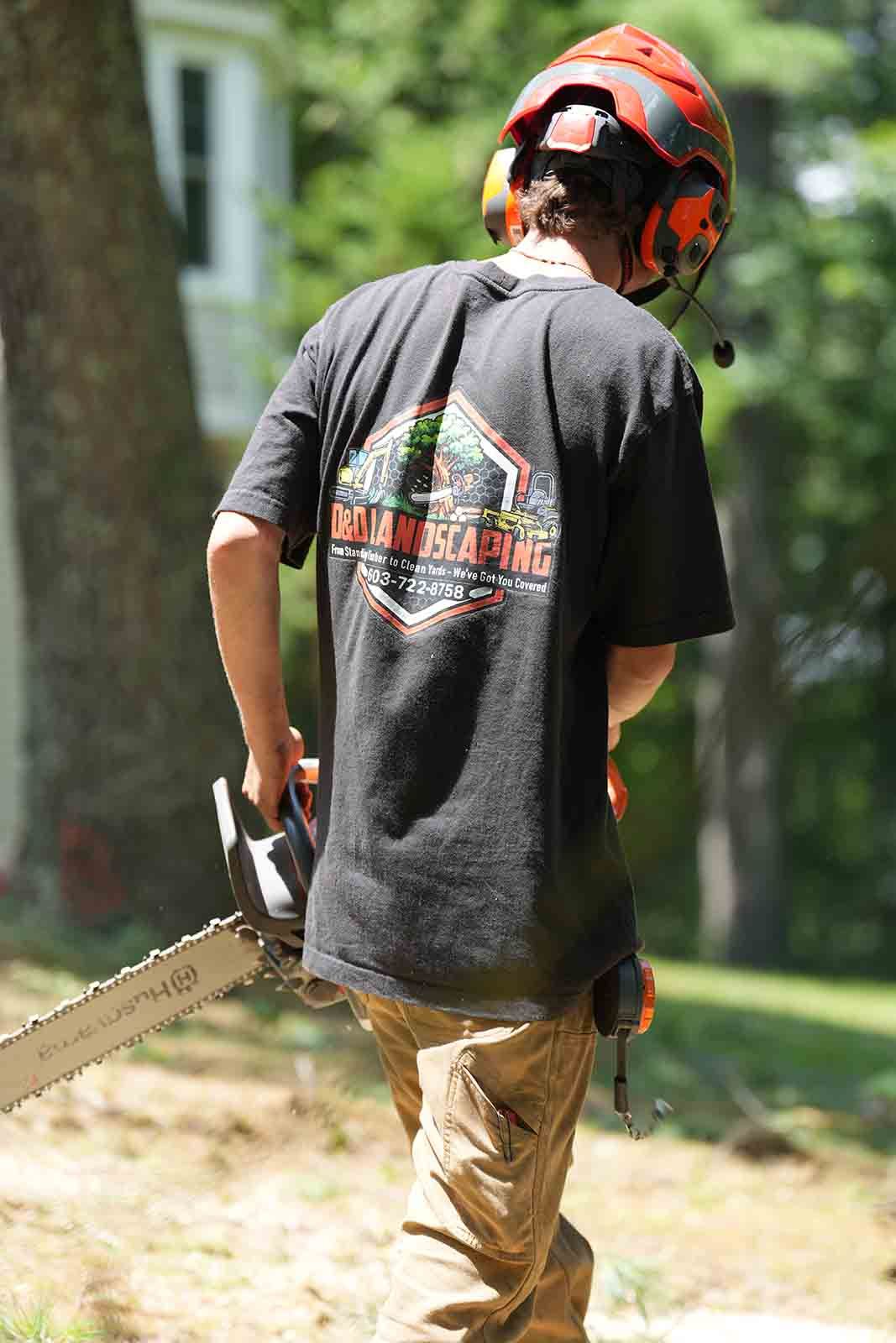 Person in orange helmet using a chainsaw outdoors near a tree and grassy yard