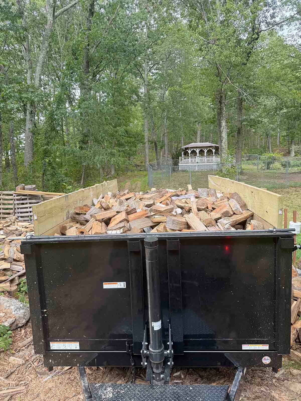 Black dumpster filled with broken bricks in a wooded outdoor area