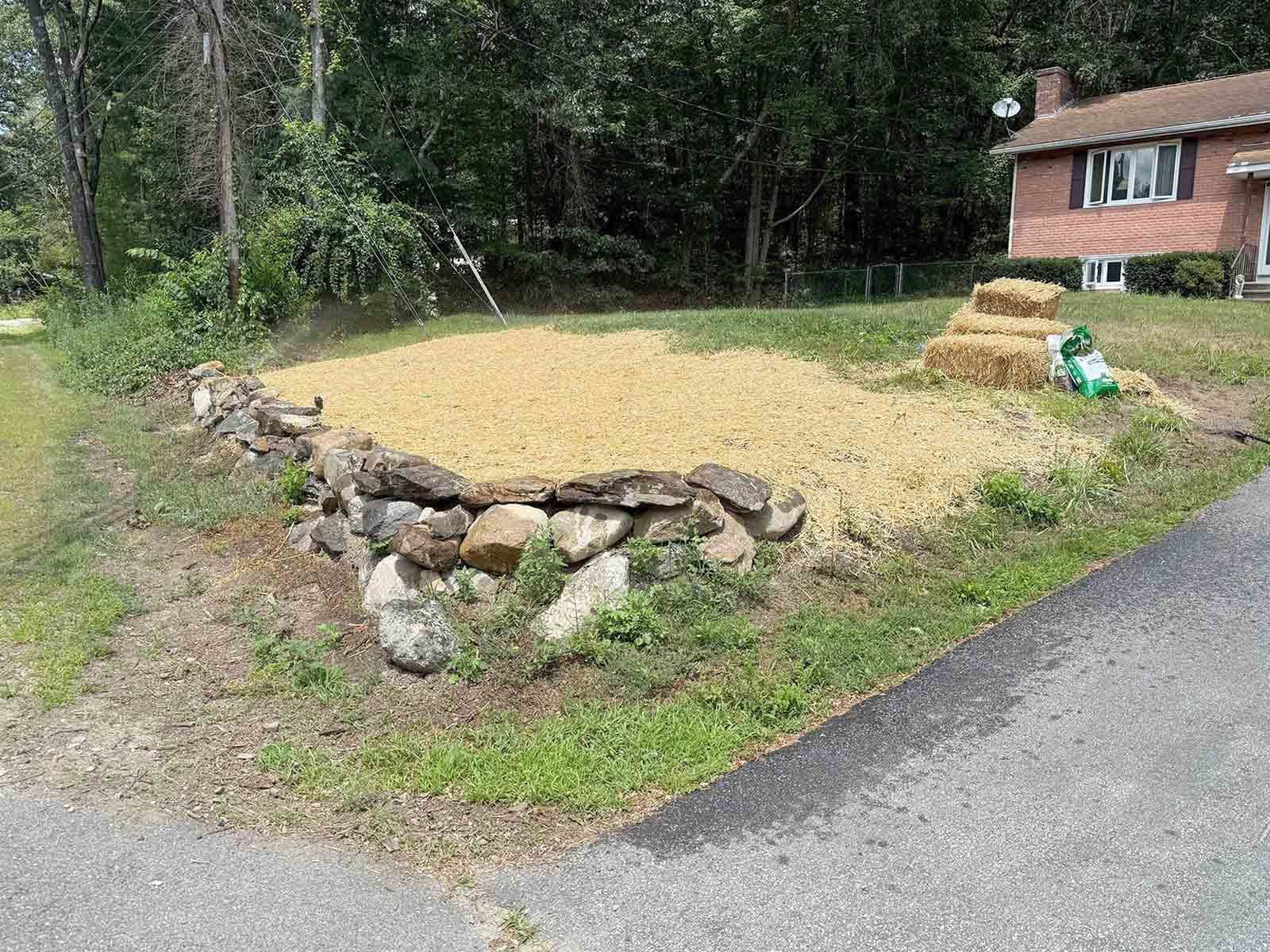 Gravel driveway edge with a low stone border beside a brick house and wooded yard