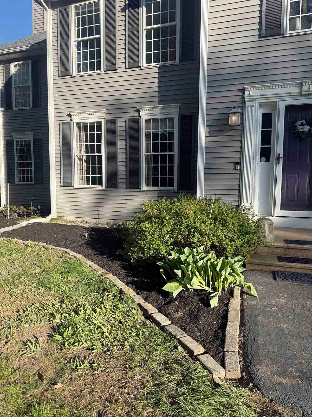 Front of a gray house with white-trimmed windows, a black door, and a small shrub-lined walkway