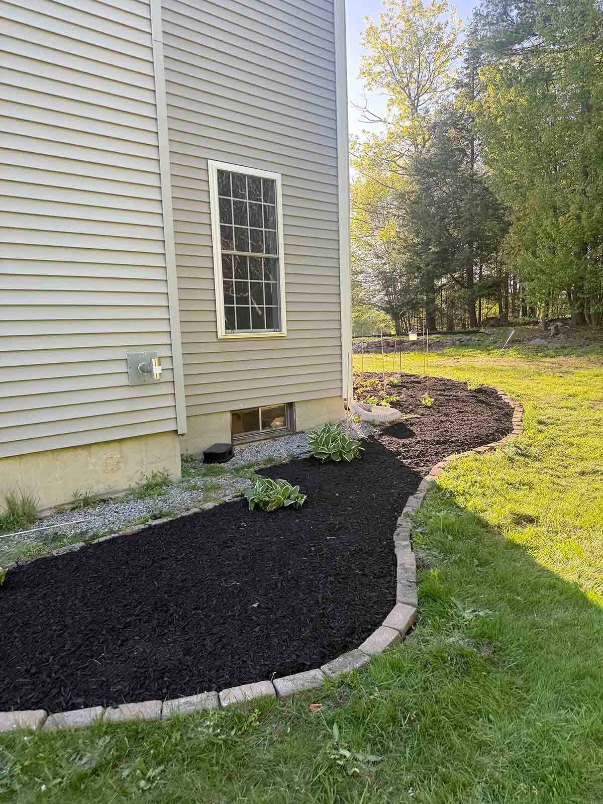 House siding beside a curving black gravel path bordered by stone and green lawn