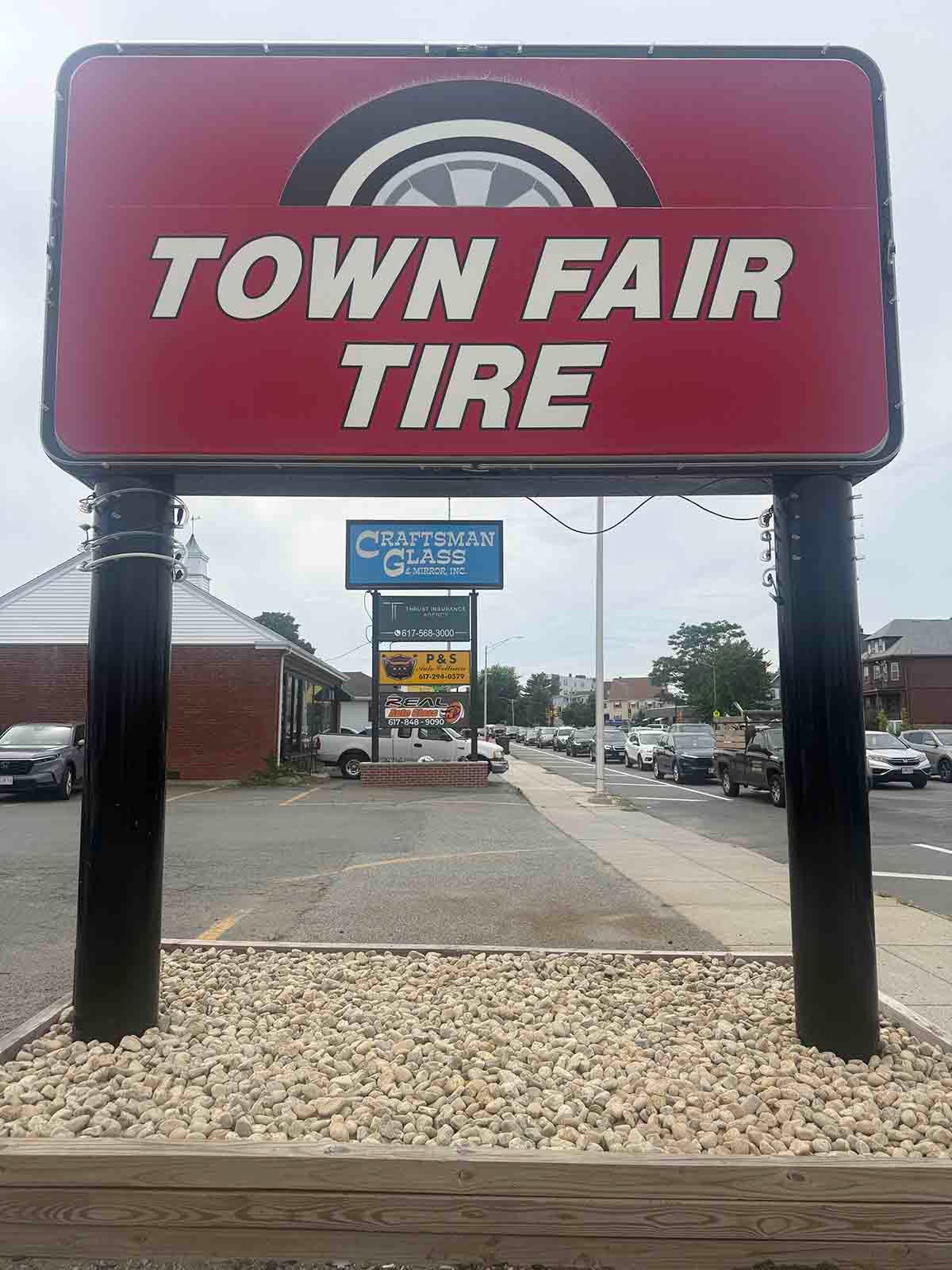 Red Town Fair Tire sign above a gravel lot beside a street and buildings