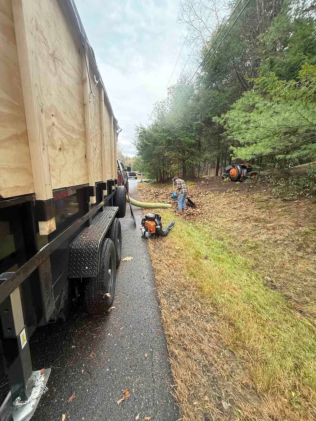 Workers clearing brush beside a truck on a gravel roadside in a wooded area.