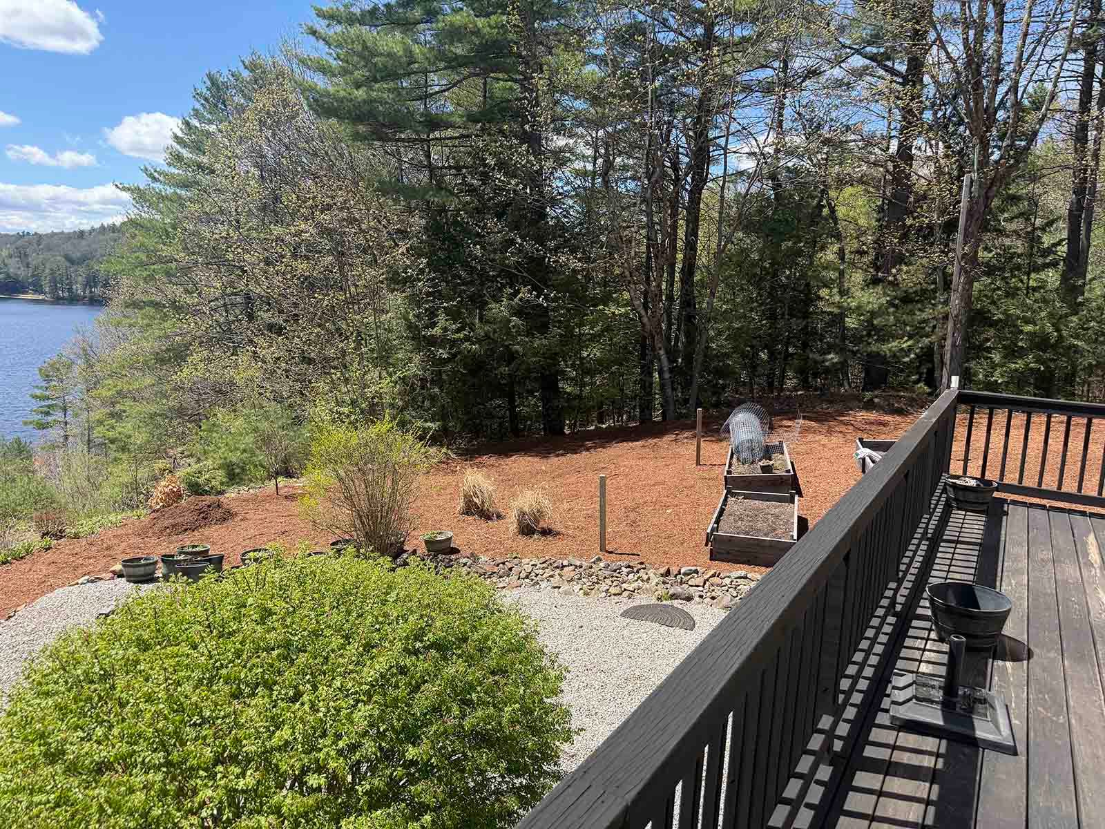Lakefront deck with black railing, stone fire pit, and trees beside a blue lake