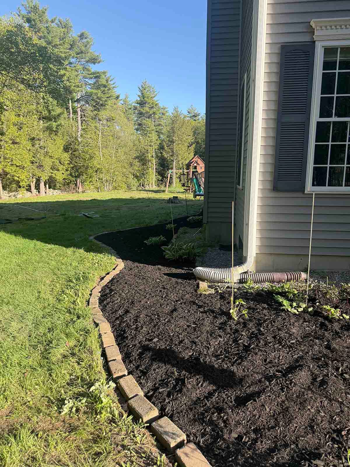 Fresh mulch bed along a house exterior beside a curved stone border and grassy yard.