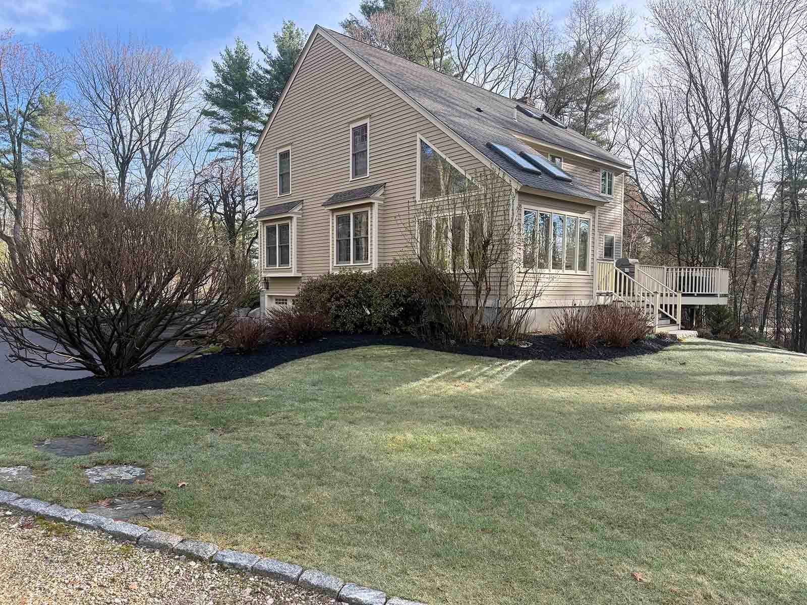 Tan house with large windows and a small porch beside a grassy yard and leafless trees