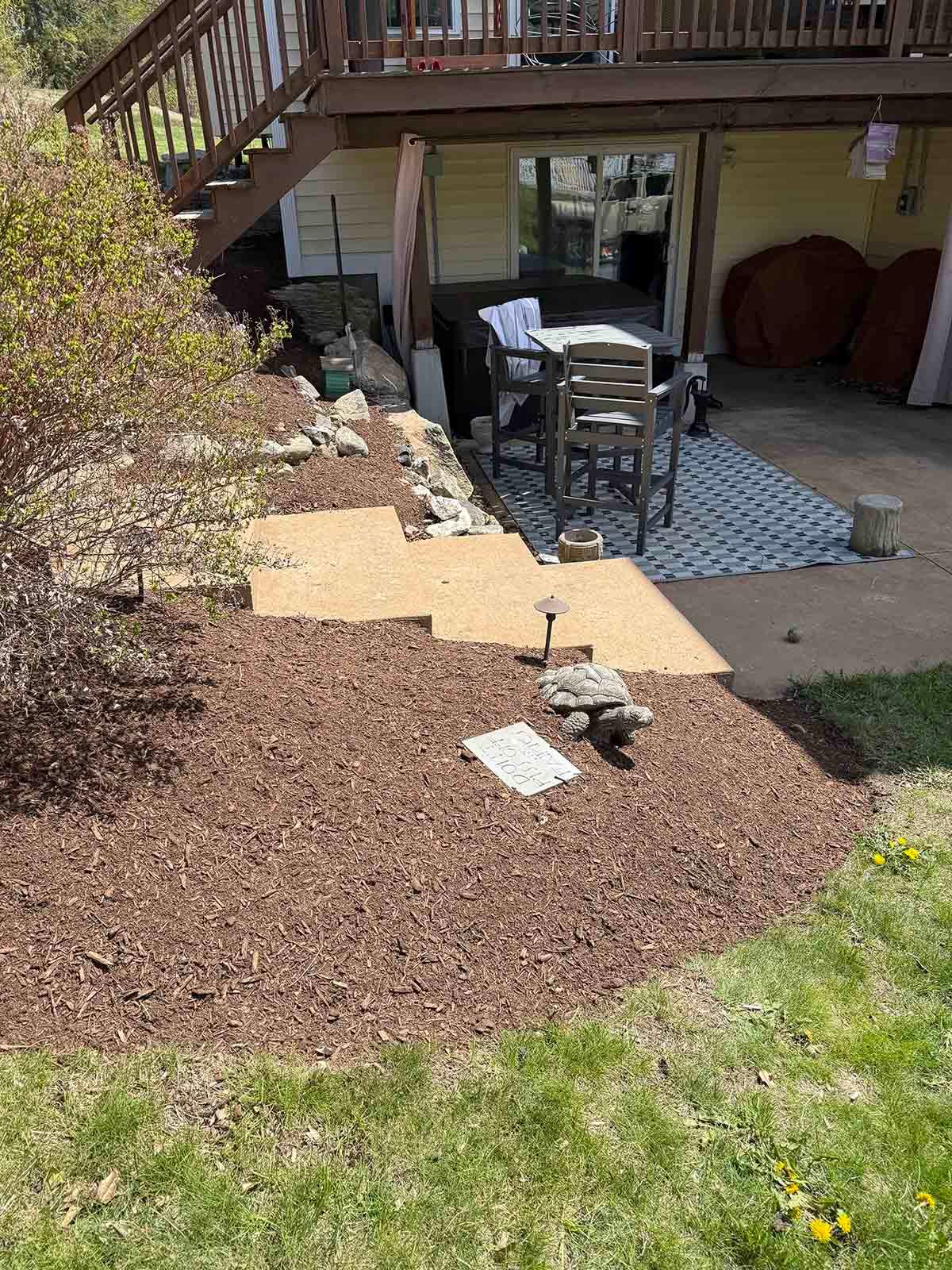 Backyard patio with chairs, table, and mulch garden bed beside a deck and house.