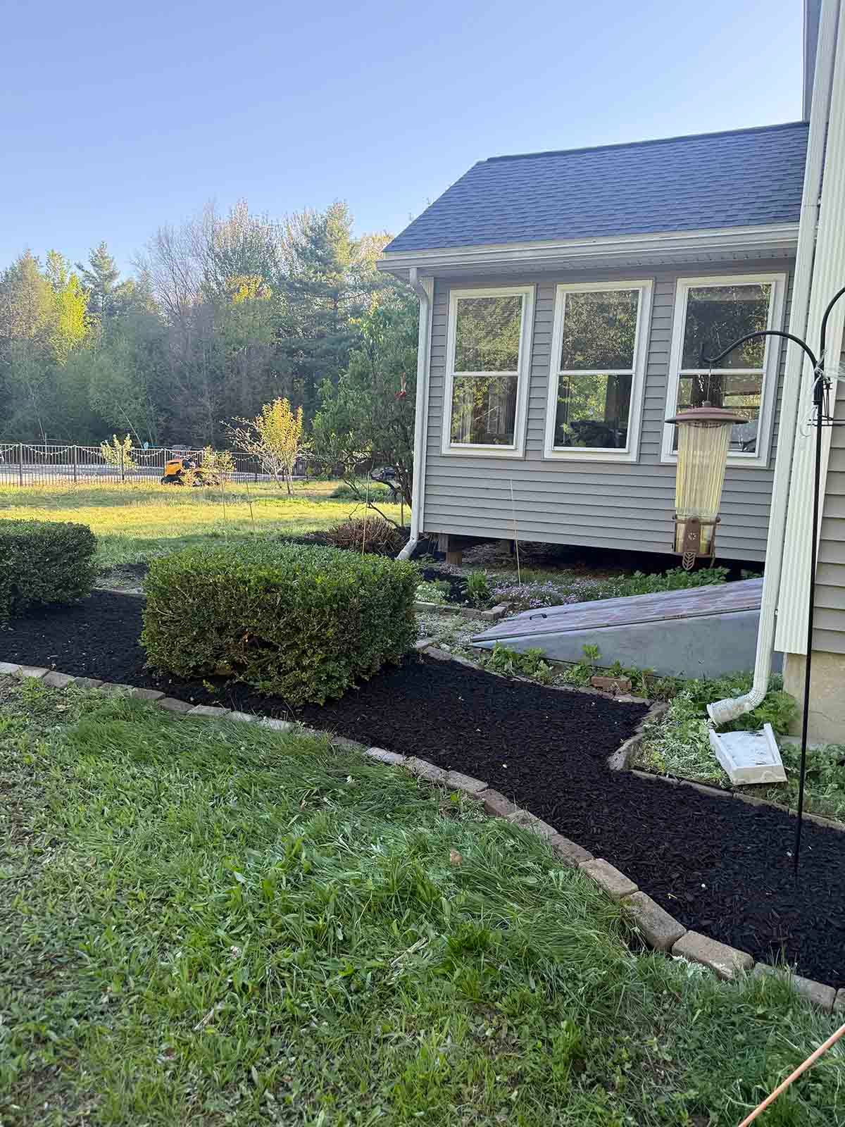 Small house with a curved black walkway, trimmed hedges, and a grassy yard in daylight