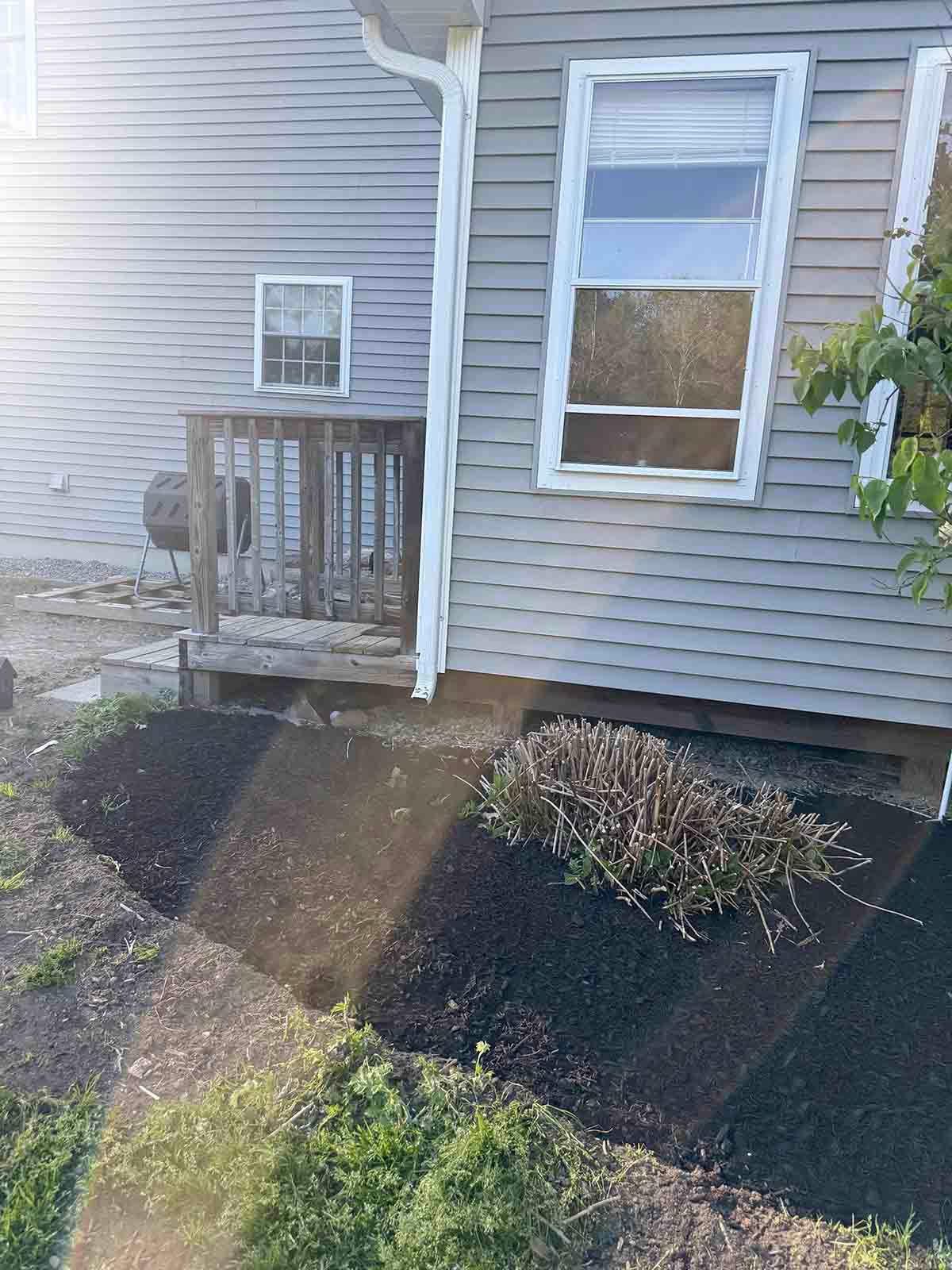 Small porch beside a gray house with white trim, front walkway, and garden beds in the yard