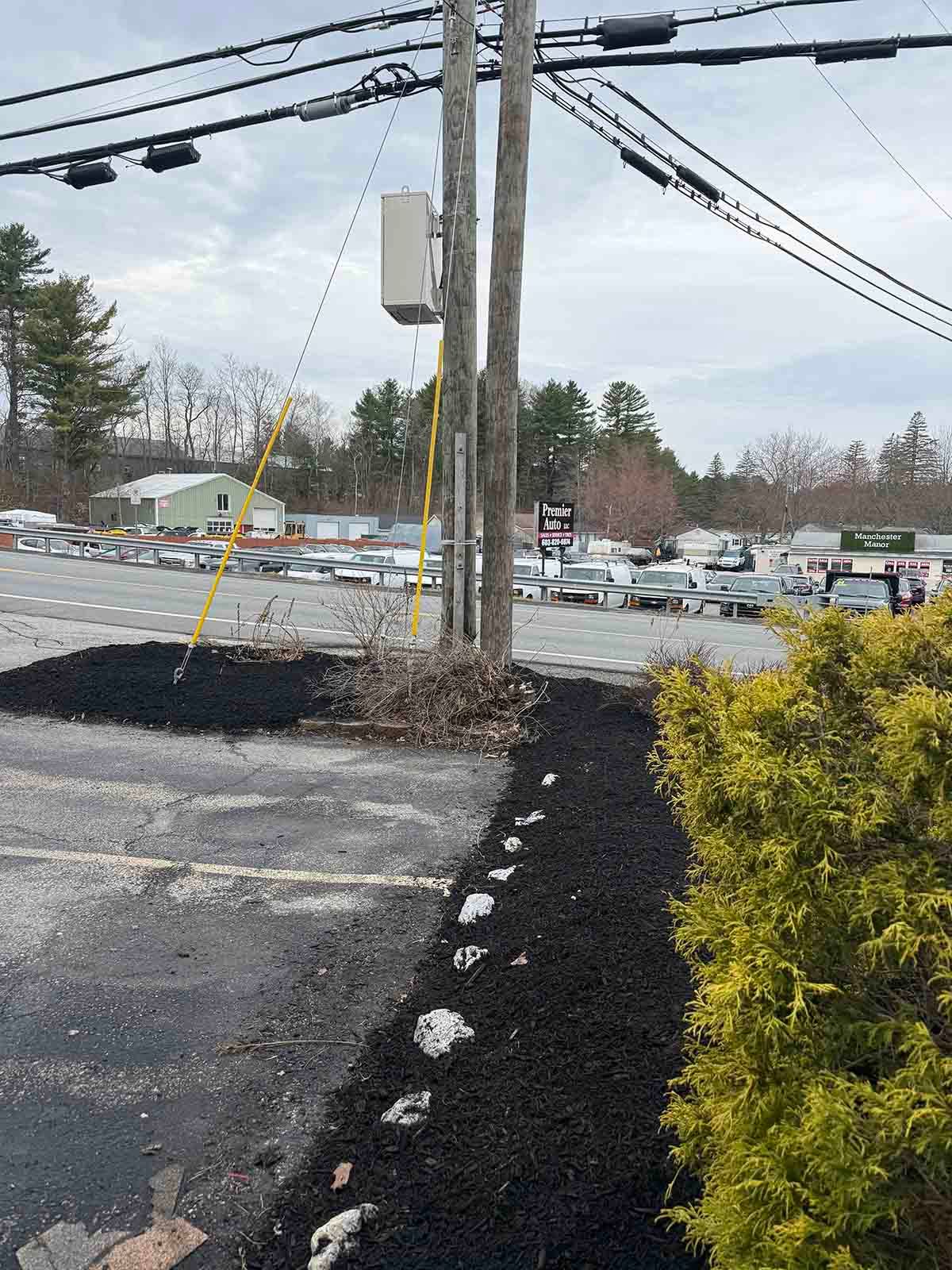 Utility pole by snowy parking lot with black mulch border and overcast sky