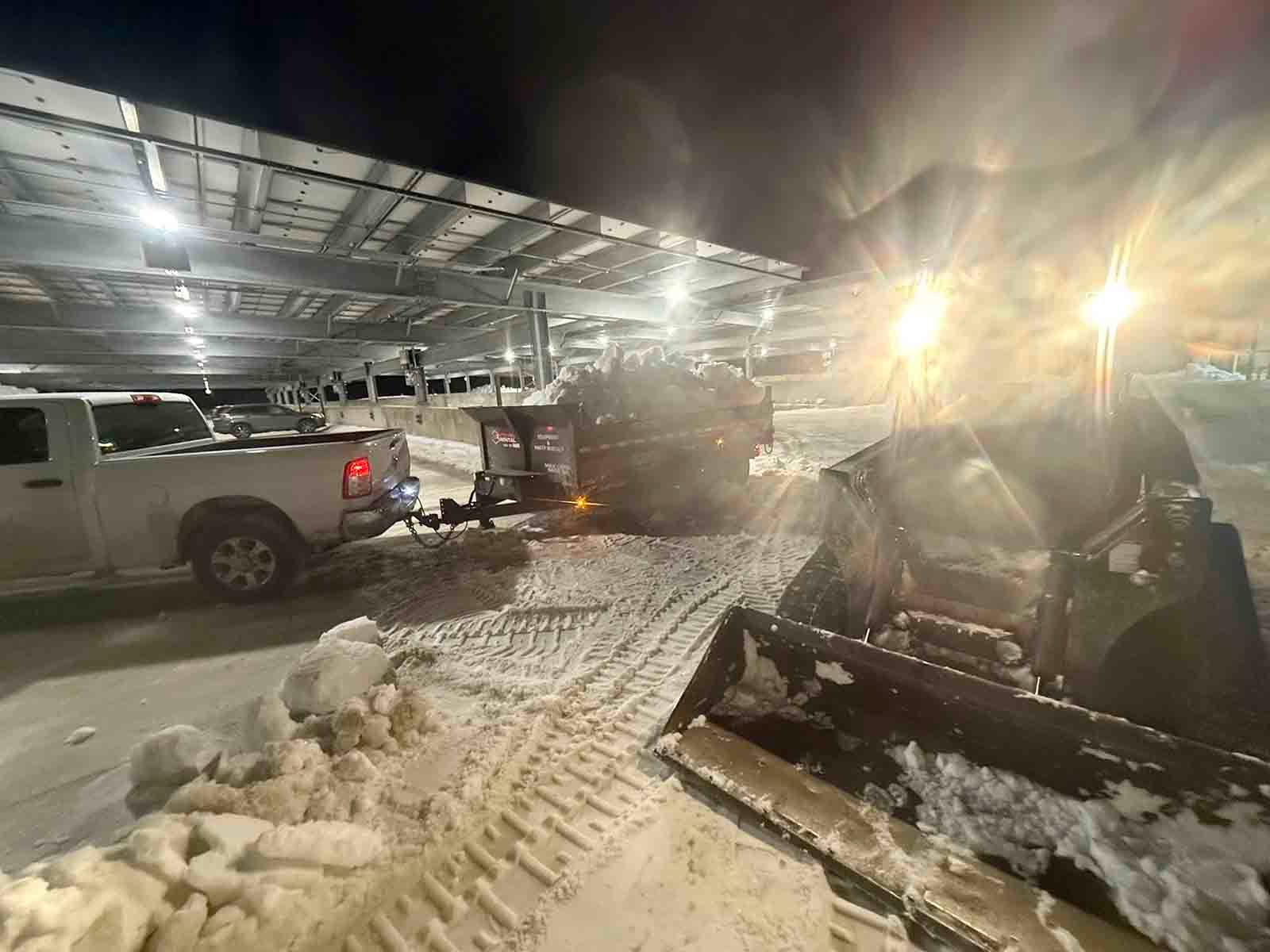 Snowy parking lot with a pickup truck and a damaged vehicle under bright lights at night