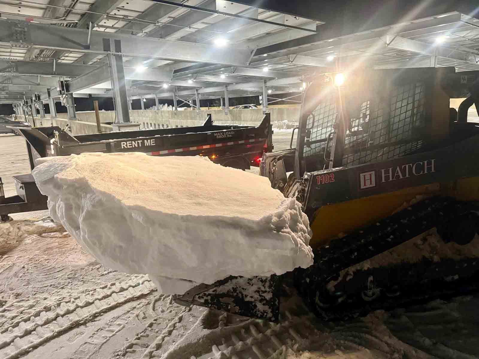 Snowplow pushing a large mound of snow inside a lit warehouse