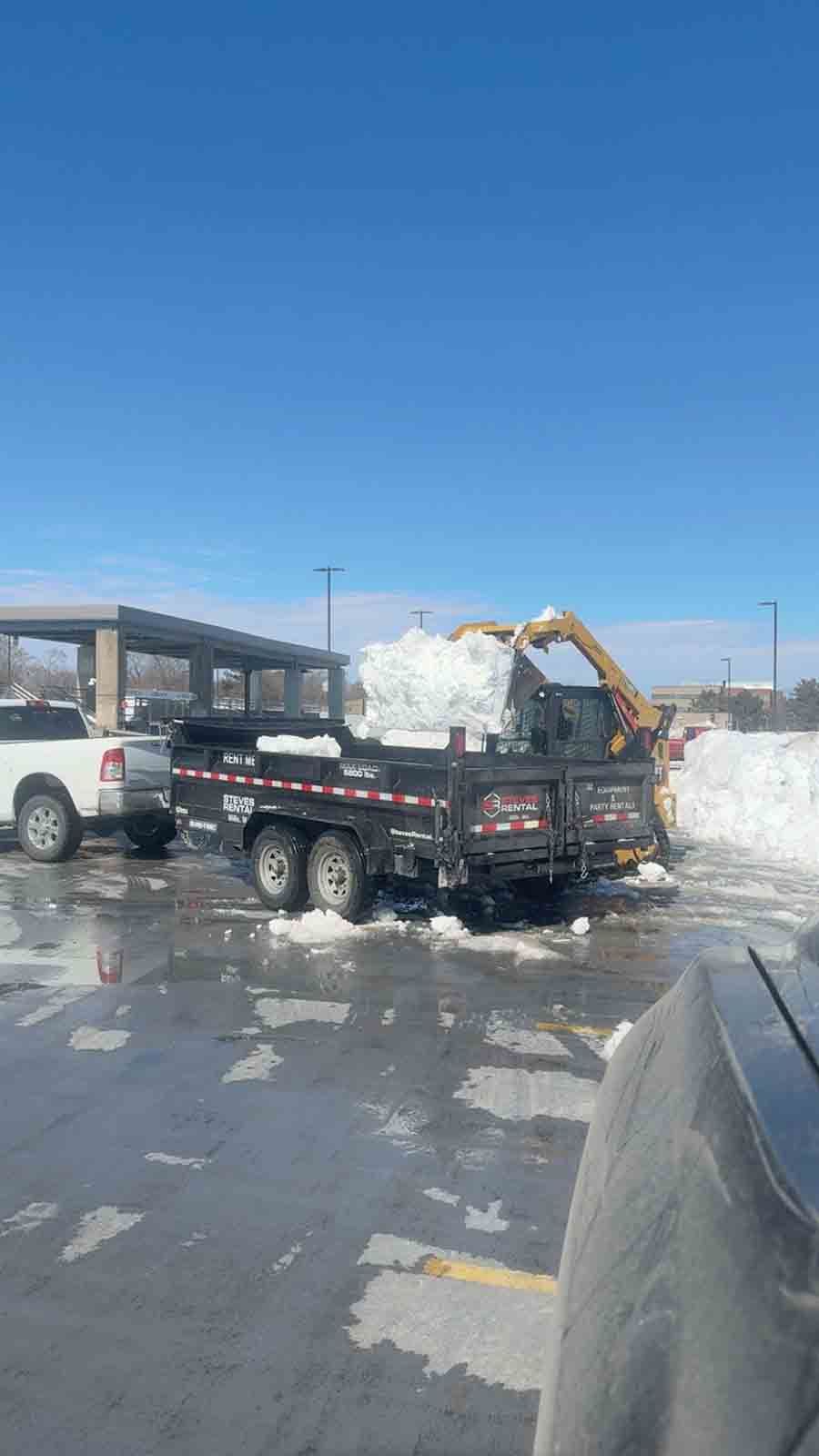 Pickup truck hauling snow-covered material in a snowy parking lot under a blue sky