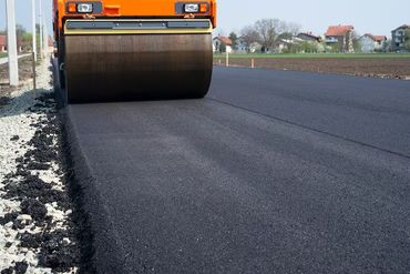 Orange road roller compacting fresh asphalt on a newly paved road