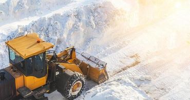 Yellow bulldozer clearing snow on a bright snowy road, viewed from above