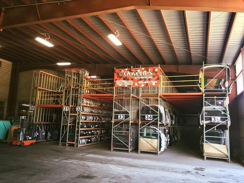 Warehouse interior with metal shelving containing car parts. A forklift is parked nearby.