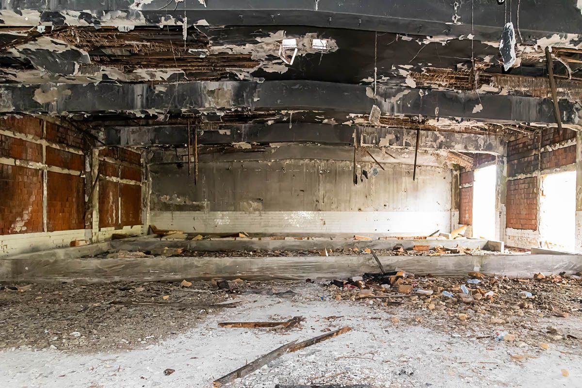 Abandoned, fire-damaged interior with a charred ceiling, debris-strewn floor, and peeling walls