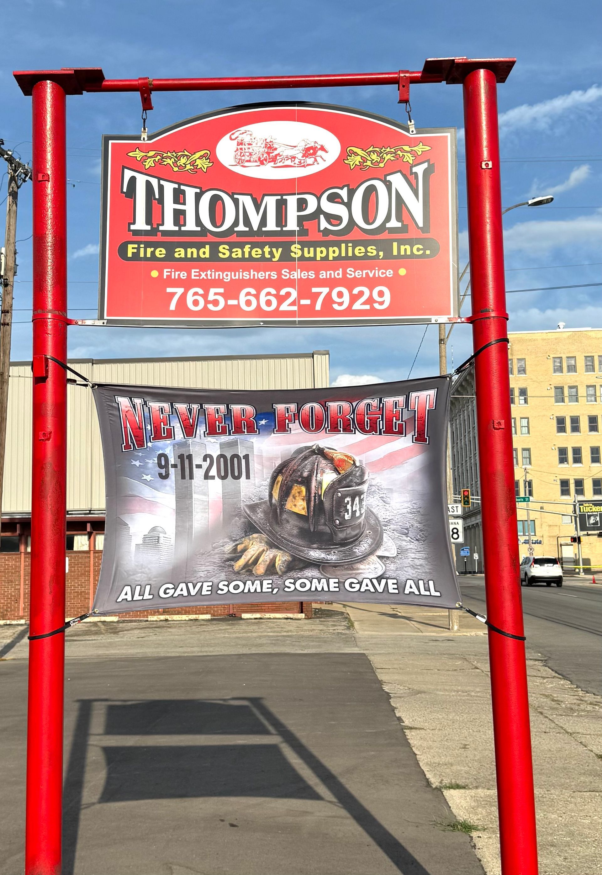 Sign for Thompson Fire & Safety Supplies with a 9/11 memorial banner in front. Red frame, sign, and banner.