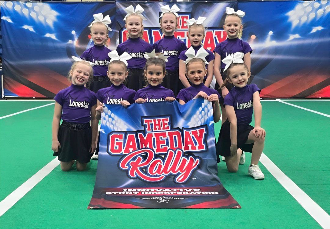 Cheer squad posing on a turf field behind a Gameday Rally sign, wearing purple uniforms.