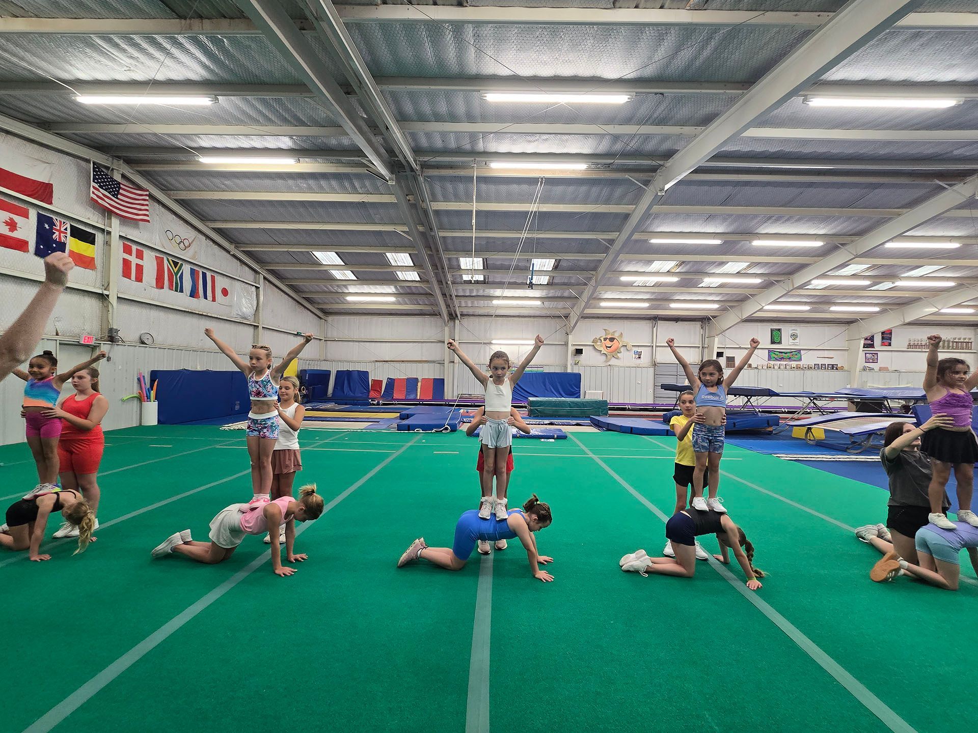 Kids practicing stunts and floor routines in a large indoor gym.