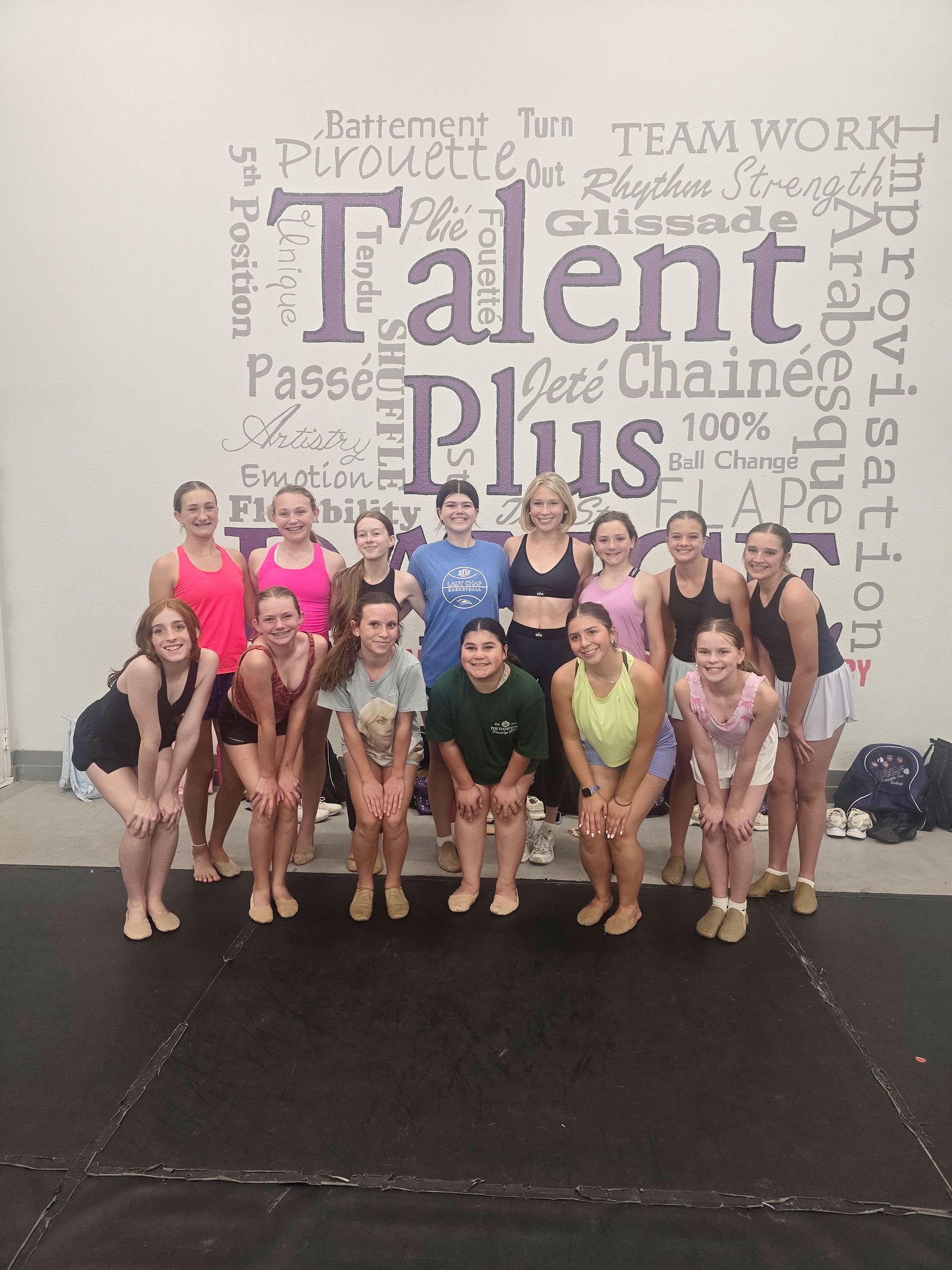 Group of dancers posing in a studio in front of a “Talent Plus” wall mural.
