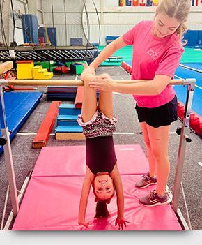 A woman is helping a little girl do a handstand on a bar.