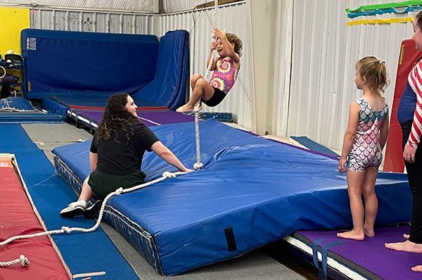 A girl is learning how to climb a rope in a gym.