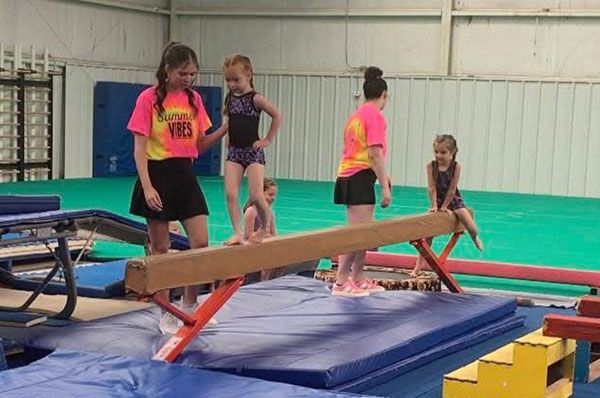 A group of young girls are standing on a balance beam in a gym.