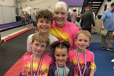 A group of children are posing for a picture with a woman in a gym.