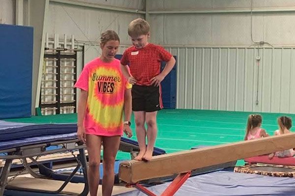 A boy and a girl are standing on a balance beam in a gym.