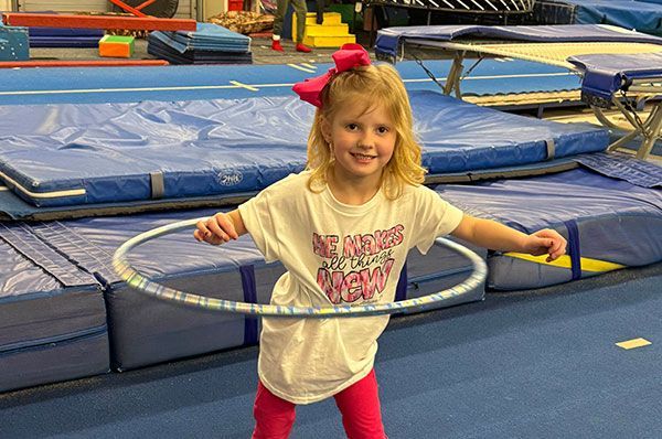 A little girl is playing with a hula hoop in a gym.