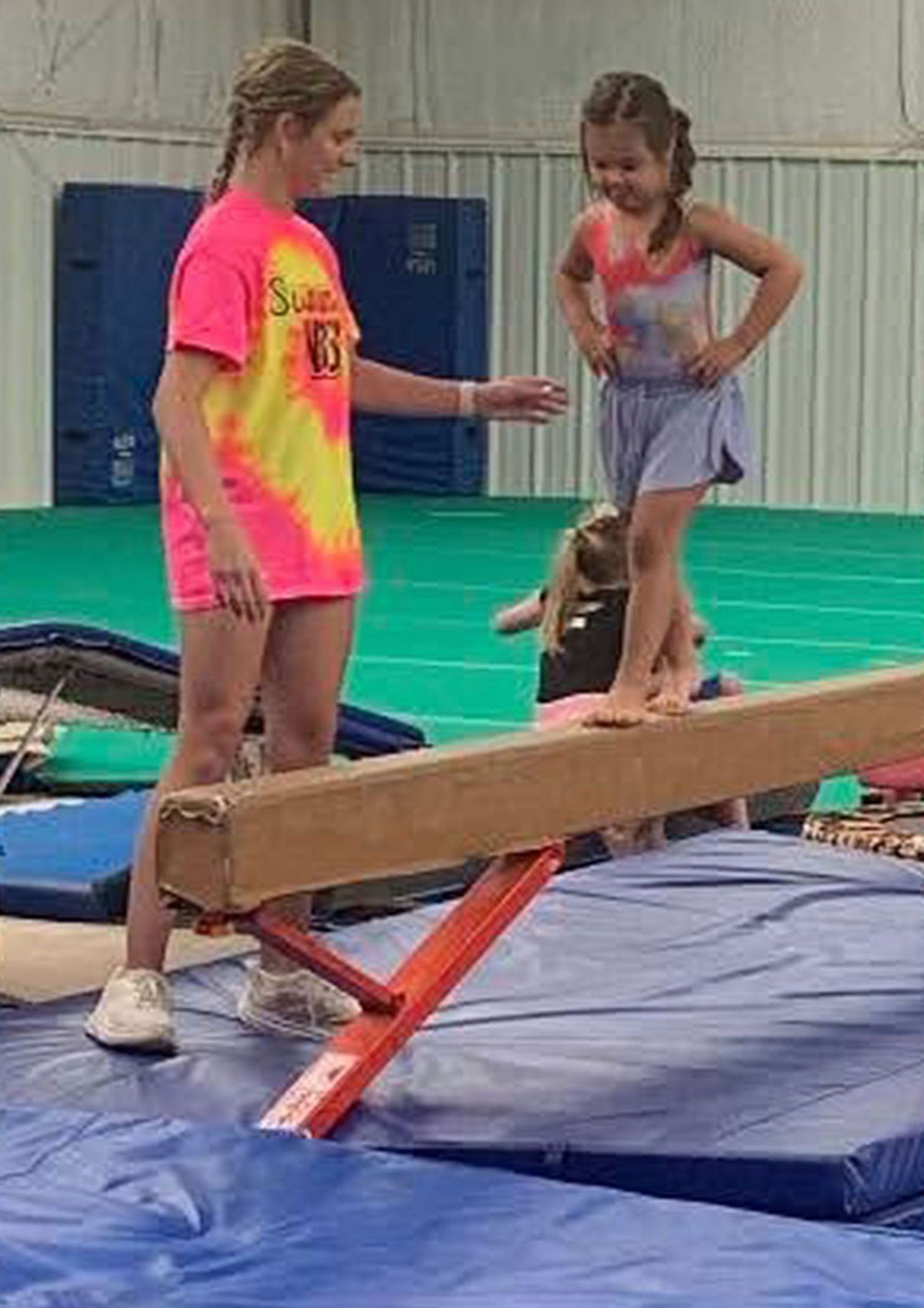 Child balancing on a beam while another child spots her in a gymnasium