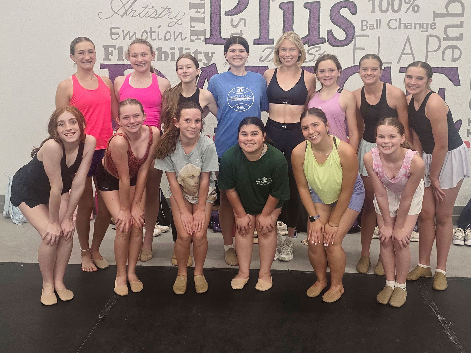 Group of dancers posing in leotards and leggings in a studio, smiling at the camera.