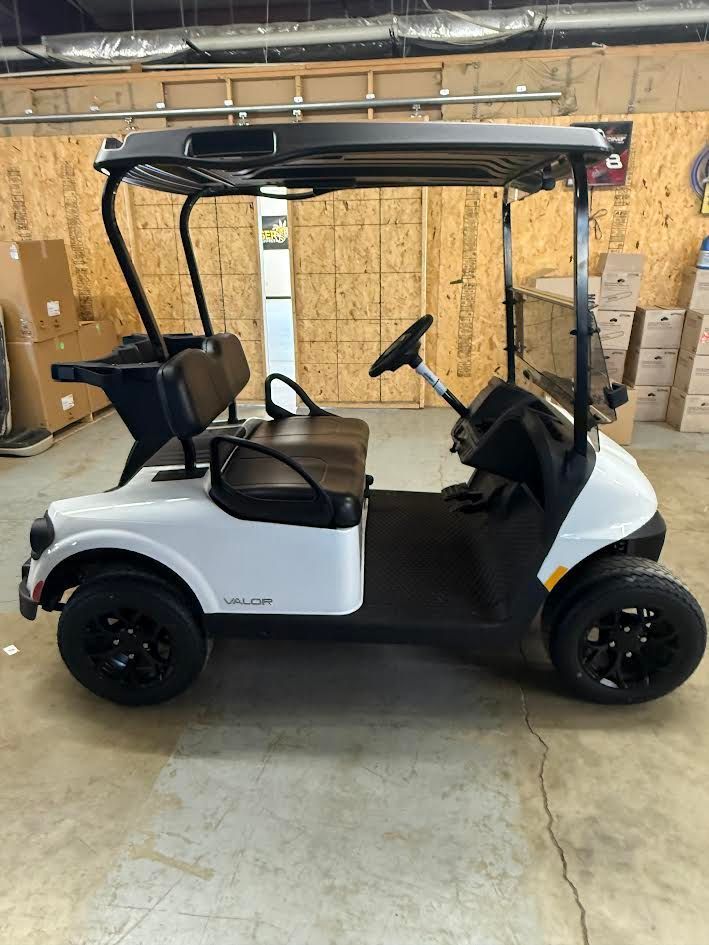 White and black golf cart with roof parked indoors in a warehouse-like space.