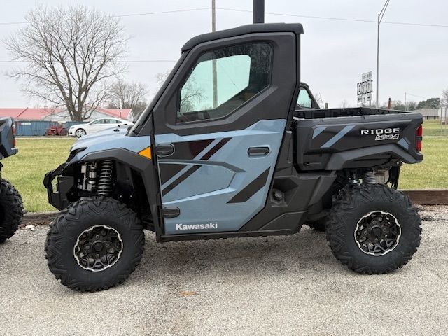 Black Kawasaki Ridge side-by-side off-road vehicle on gravel, with large tires and blue-gray doors.