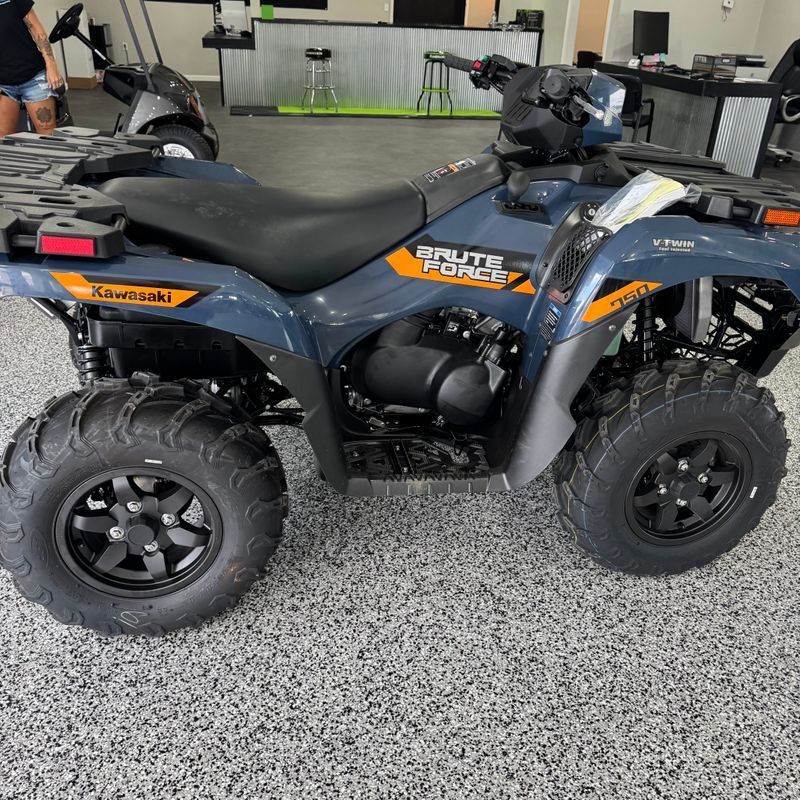 Blue-gray ATV parked indoors on a speckled floor, side view with black seats and chunky tires