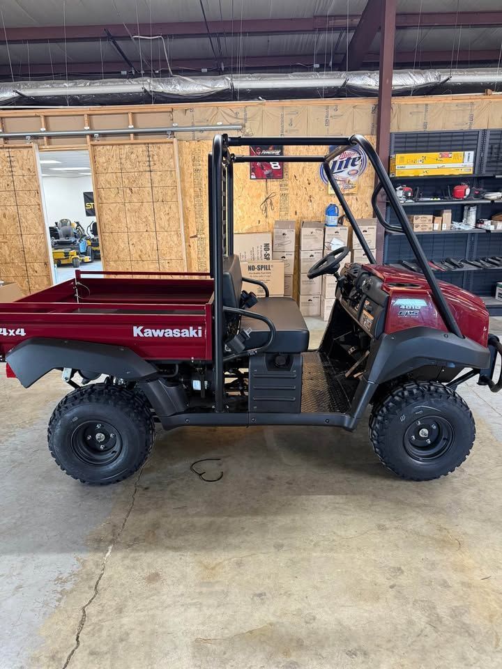 Red Kawasaki utility side-by-side parked in a workshop garage with concrete floor.