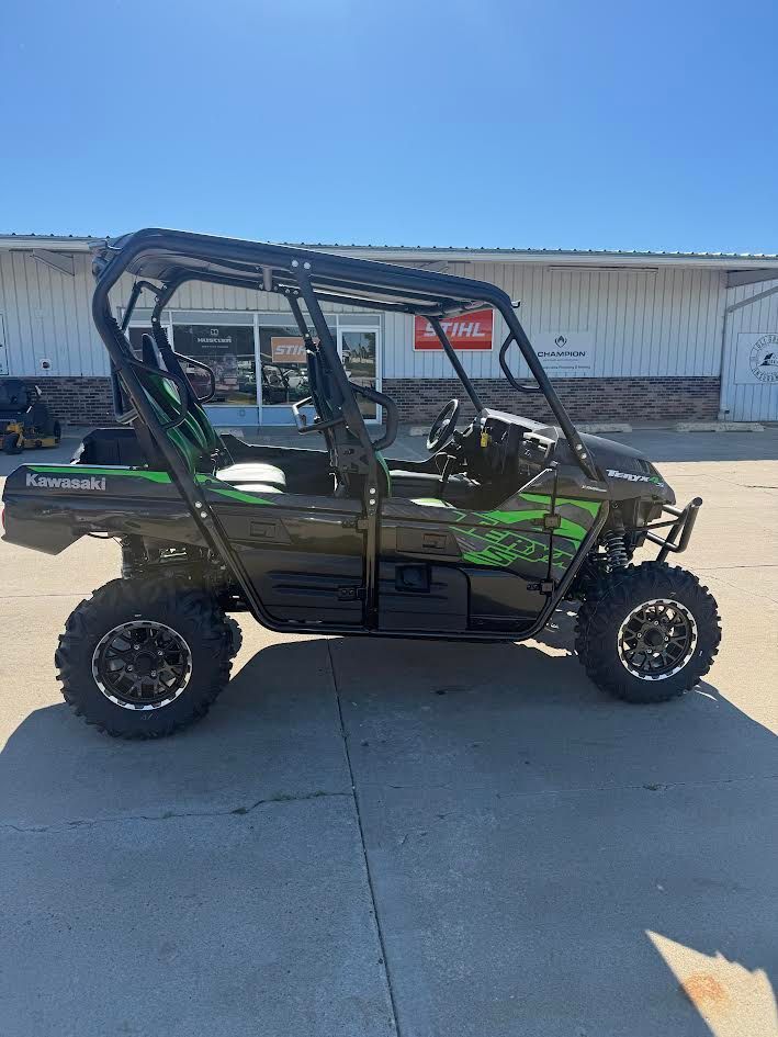 Black and green side-by-side UTV parked on a concrete lot in front of a warehouse under a blue sky