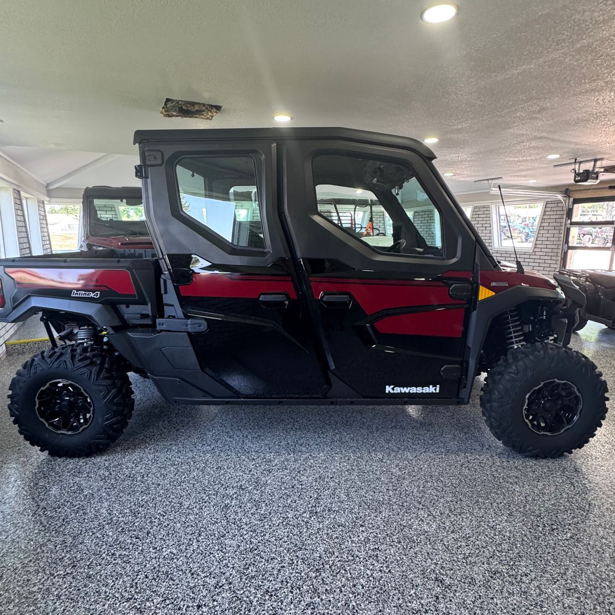 Black and red Kawasaki side-by-side utility vehicle parked indoors on a speckled floor
