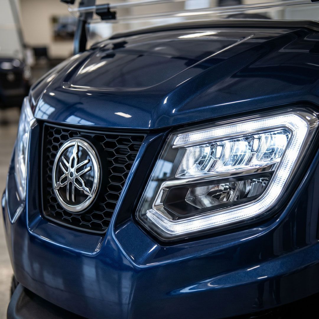 Close-up of a blue truck front grille and headlight with a silver emblem