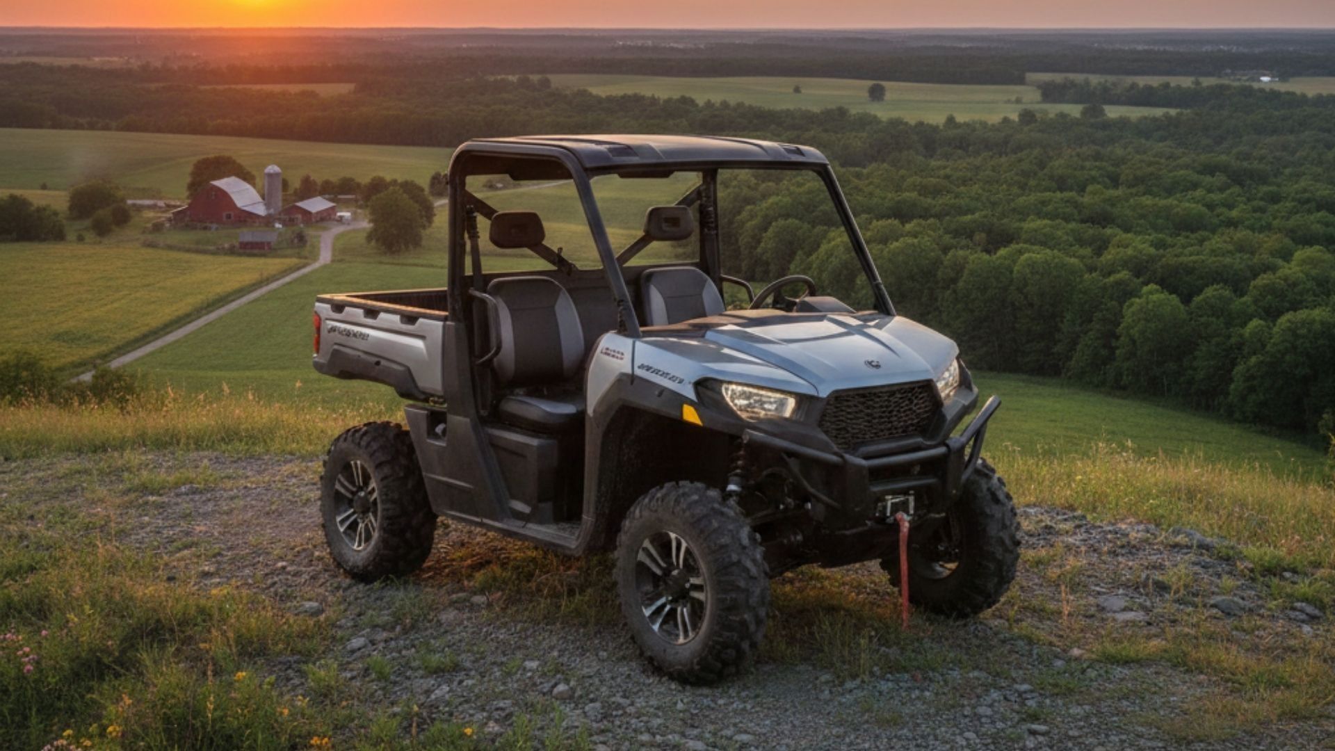Black off-road utility vehicle on a grassy hill at sunset, overlooking a wooded valley.