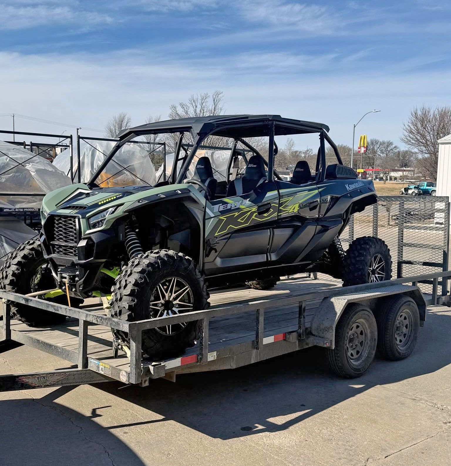 Damaged green-and-black off-road side-by-side on a trailer in a parking lot