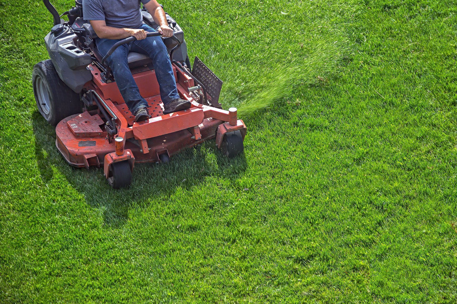 Person riding a red lawn mower across a green grassy yard