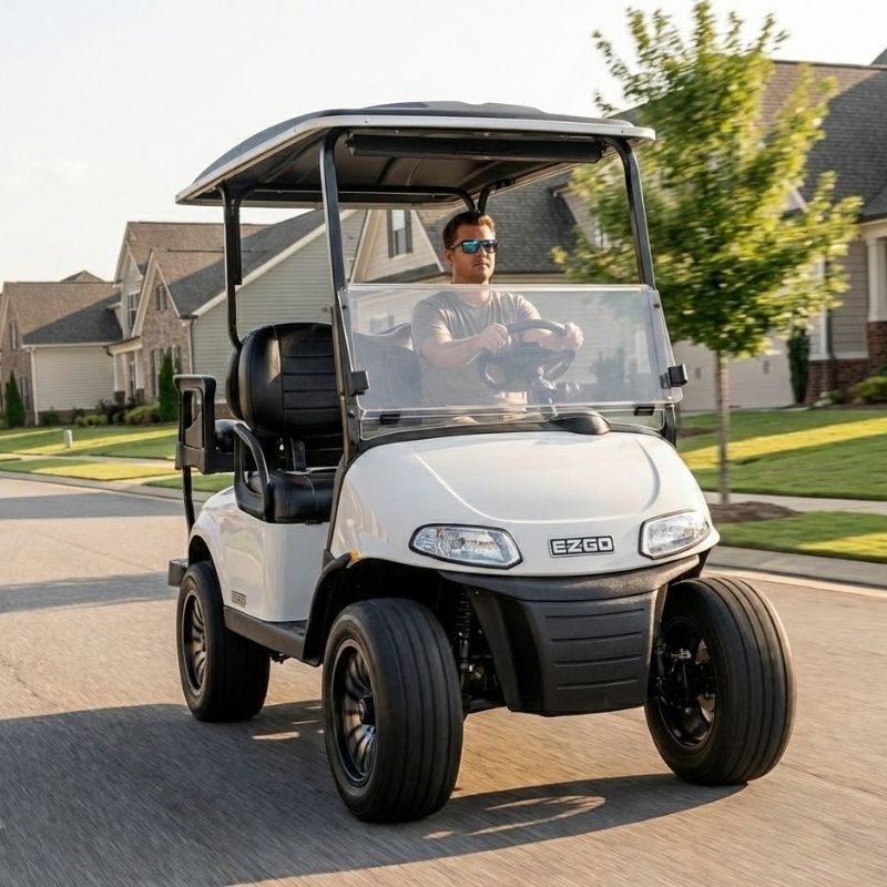 White golf cart driving on a suburban street, with a clear windshield and black roof.